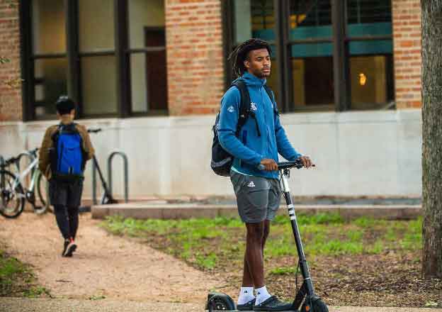 Student riding on a scooter on Rice's campus.