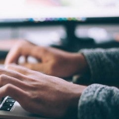 Hands typing on a keyboard, illuminated by the screen.