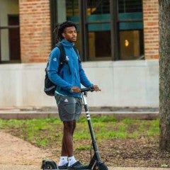 Student riding on a scooter on Rice's campus.
